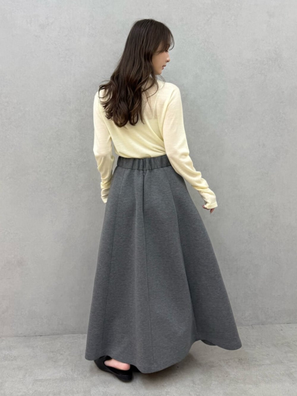 イエロー系のニット/セーター、グレー系のスカート、ブラック系のパンプスを着用したレディースの冬コーディネートの3枚目の写真