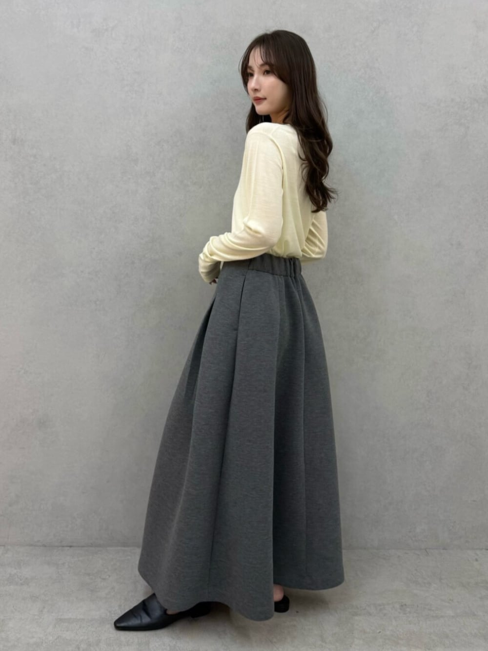 イエロー系のニット/セーター、グレー系のスカート、ブラック系のパンプスを着用したレディースの冬コーディネートの2枚目の写真
