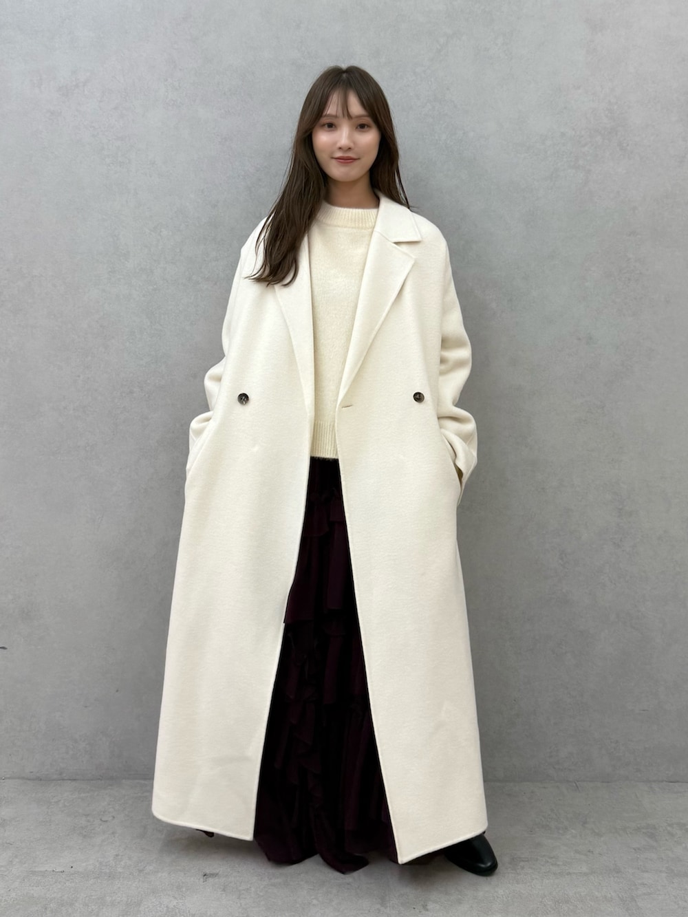 ホワイト系のチェスターコート、ホワイト系のニット/セーター、レッド系のスカートを着用したレディースの秋コーディネートの2枚目の写真