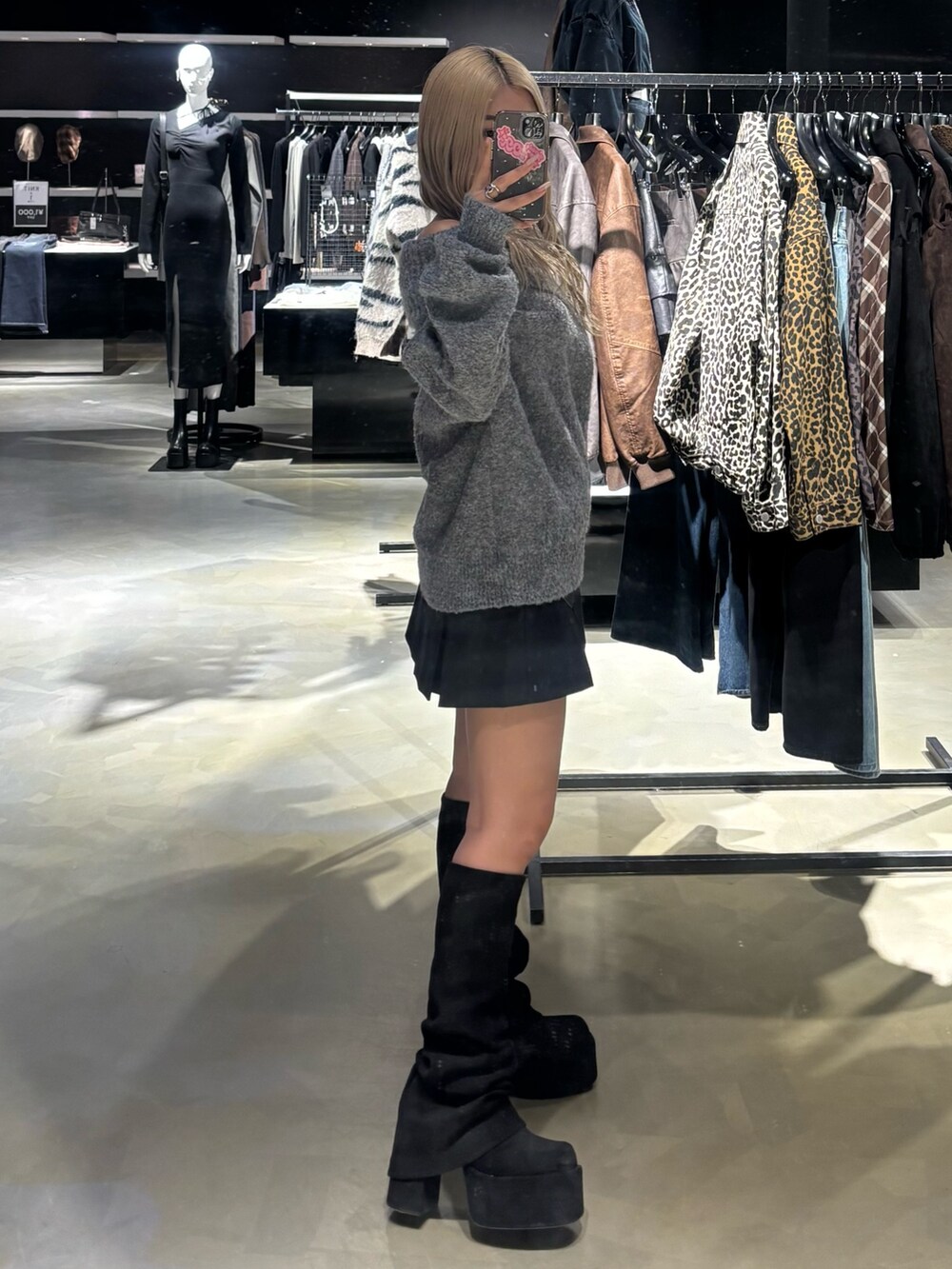 グレー系のニット/セーター、ブラック系のスカート、ブラック系のブーツを着用したレディースの秋コーディネートの2枚目の写真