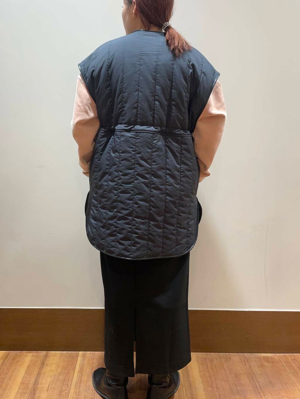 ブラック系のスカート、グレー系のダウンベスト、オレンジ系のTシャツ/カットソーを着用したレディースの冬コーディネートの3枚目の写真