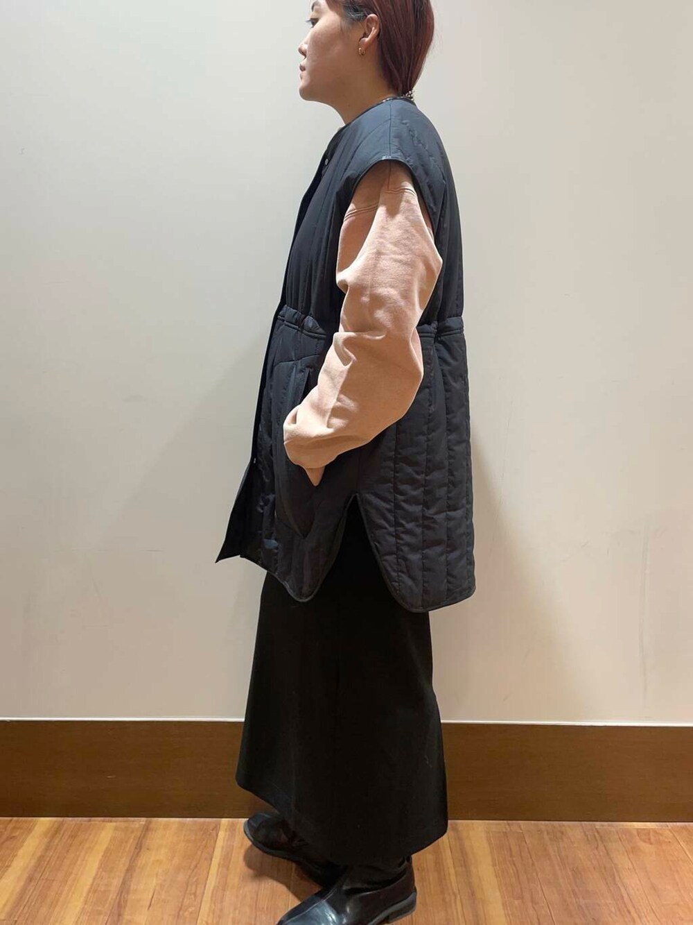 ブラック系のスカート、グレー系のダウンベスト、オレンジ系のTシャツ/カットソーを着用したレディースの冬コーディネートの2枚目の写真