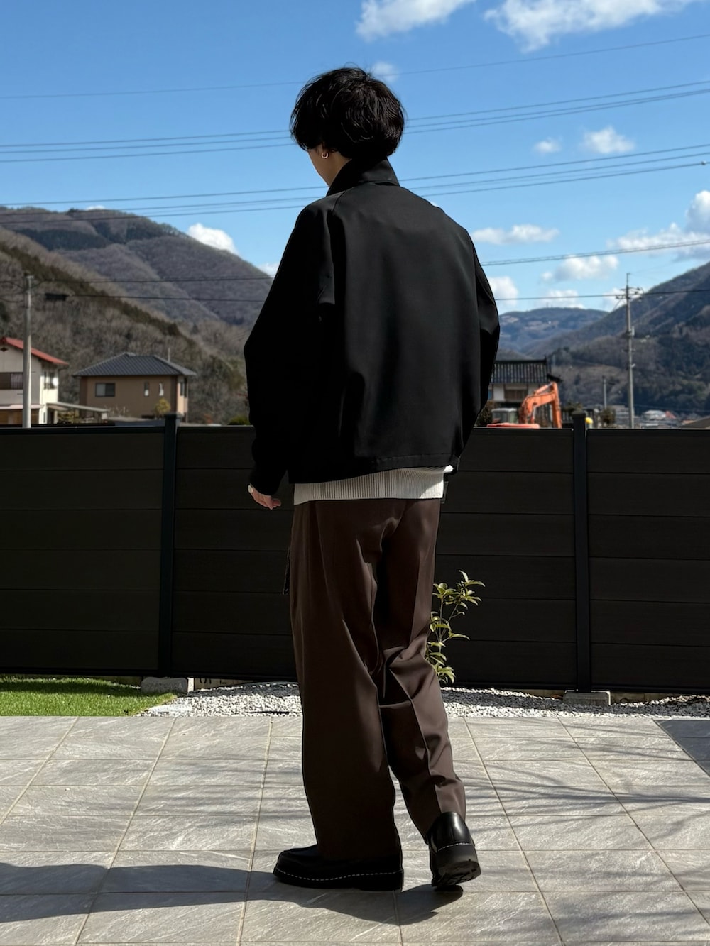 ブラック系のジャケット/アウター、ブラウン系のスラックス、ベージュ系のニット/セーターを着用したメンズの春コーディネートの2枚目の写真