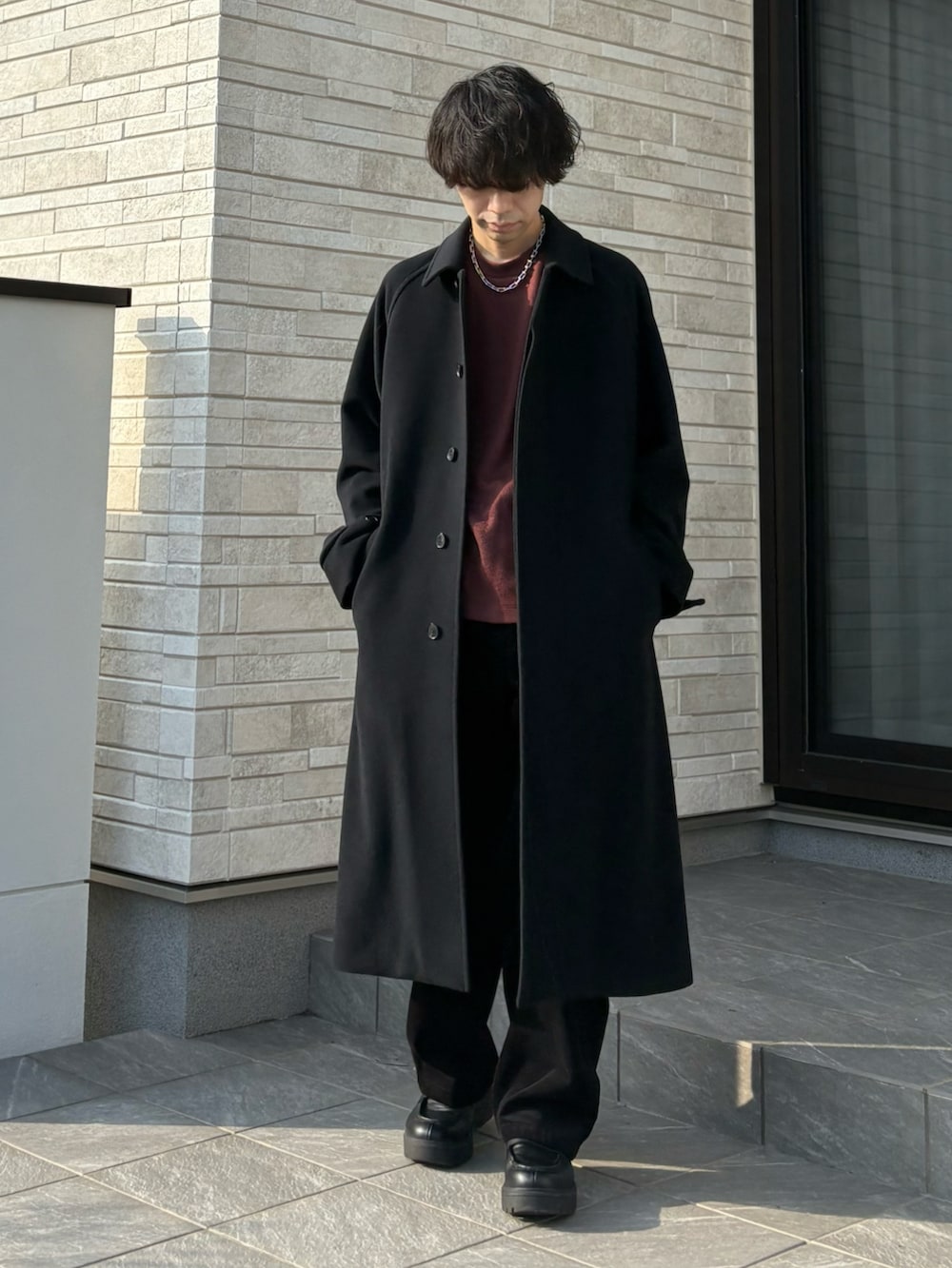 ブラック系のステンカラーコート、レッド系のニット/セーター、ブラック系のローファーを着用したメンズの冬コーディネートの2枚目の写真
