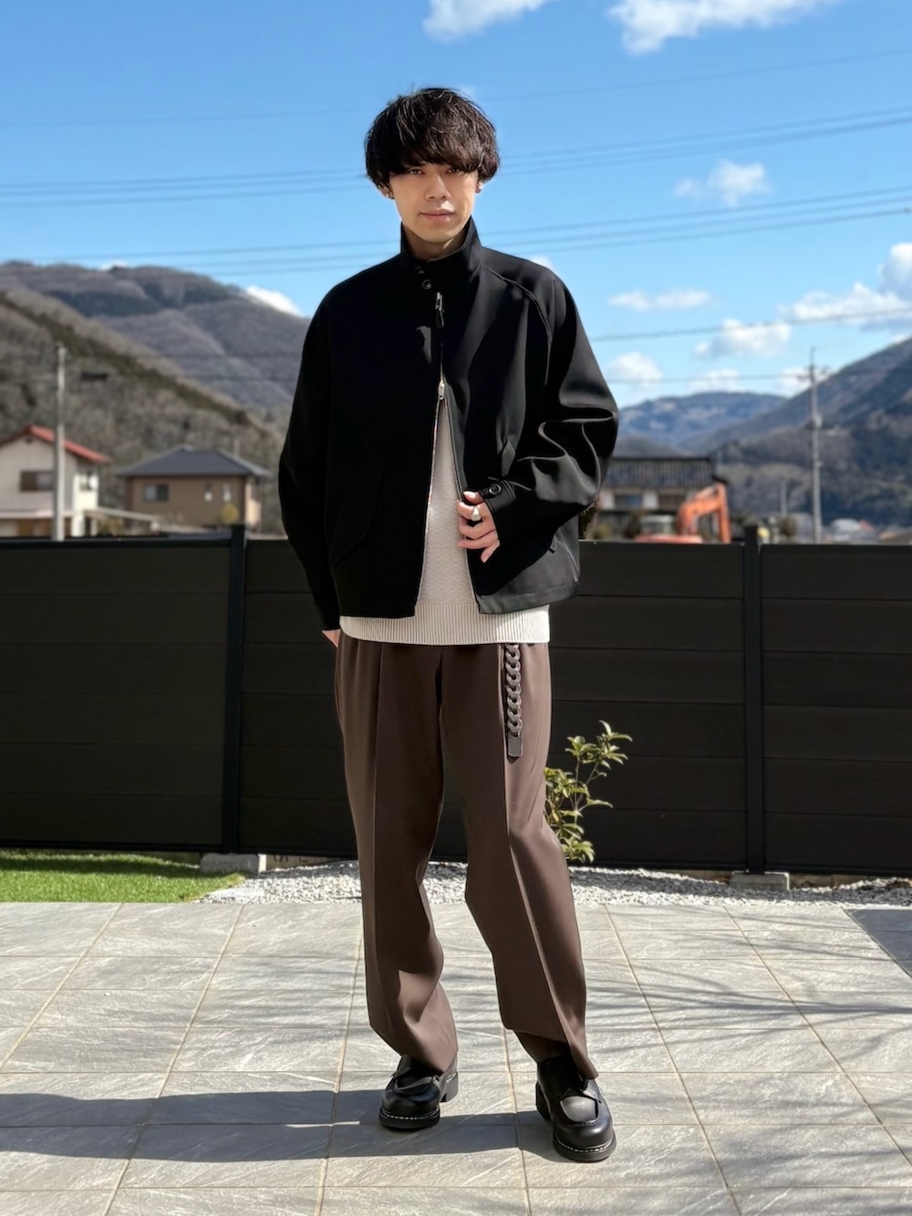 ブラック系のジャケット/アウター、ブラウン系のスラックス、ベージュ系のニット/セーターを着用したメンズの春コーディネートの3枚目の写真