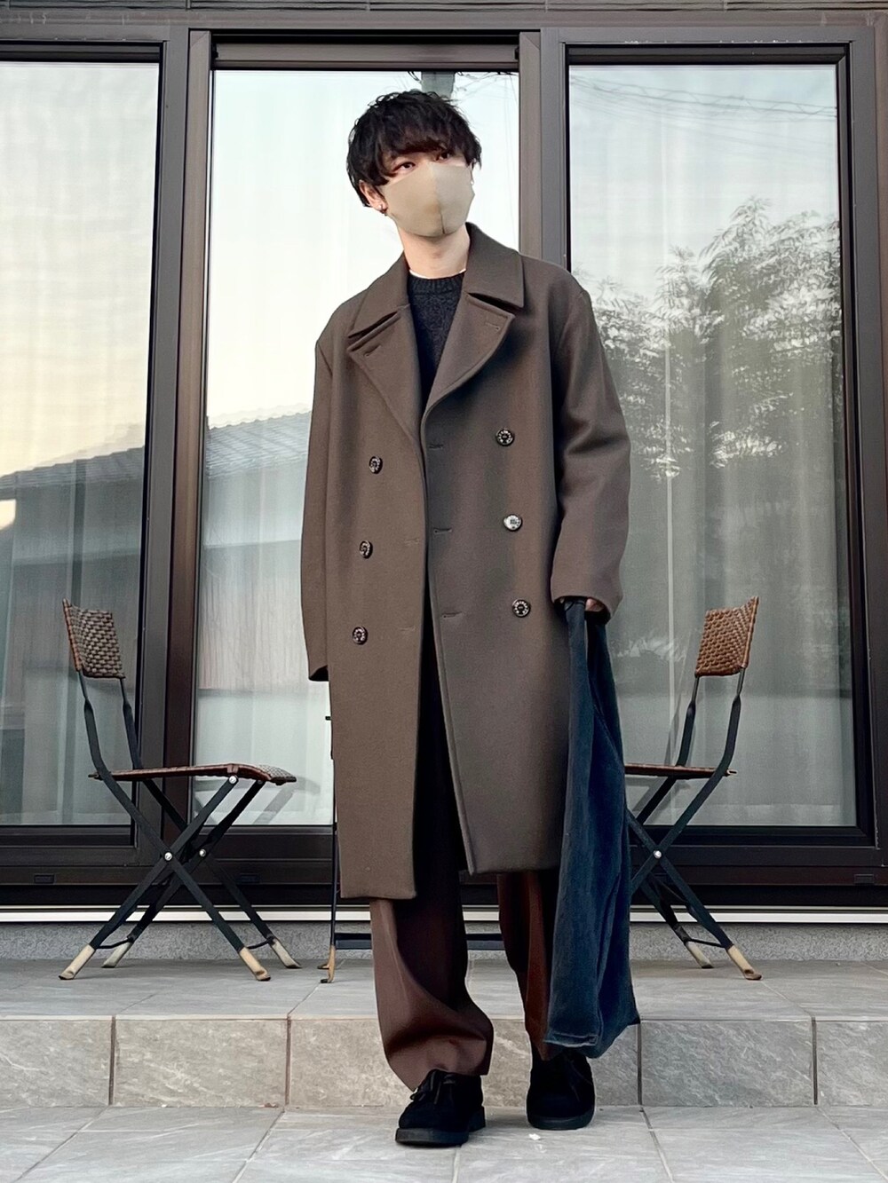 グリーン系のトレンチコート、ブラック系のブーツ、ブラウン系のスラックスを着用したメンズの冬コーディネートの2枚目の写真