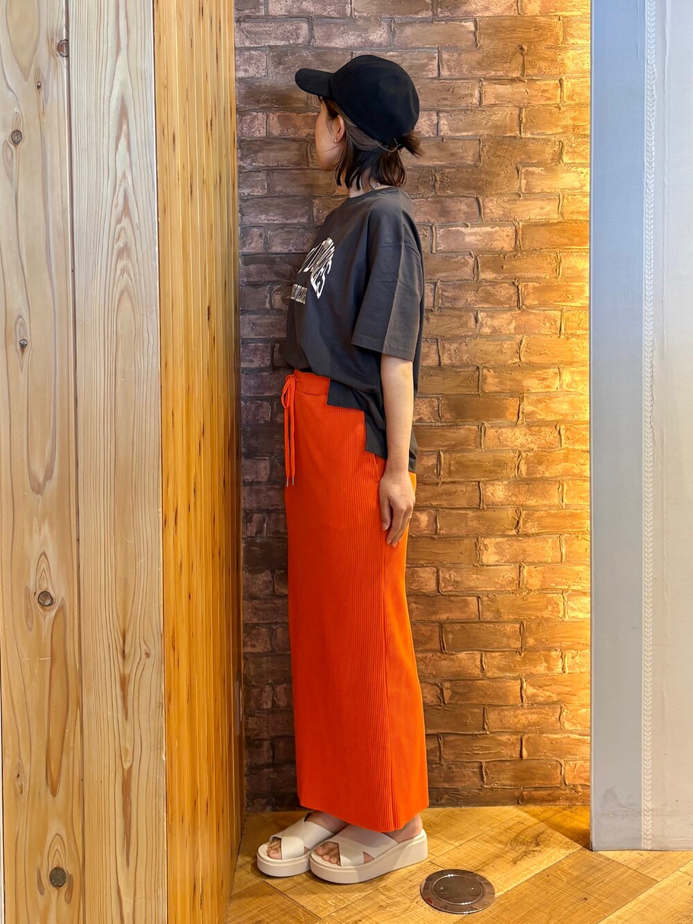 オレンジ系のスカート、ベージュ系のサンダル、ブラック系のキャップを着用したレディースの夏コーディネートの2枚目の写真