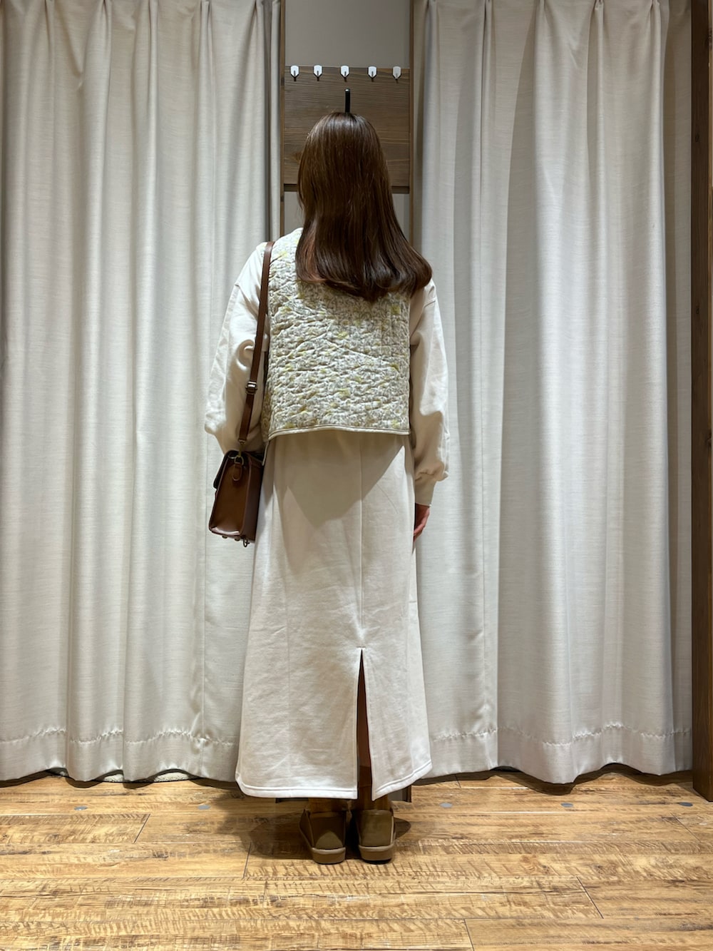 ベージュ系のベスト、ホワイト系のワンピース、ブラウン系のモカシン/デッキシューズを着用したレディースの冬コーディネートの2枚目の写真