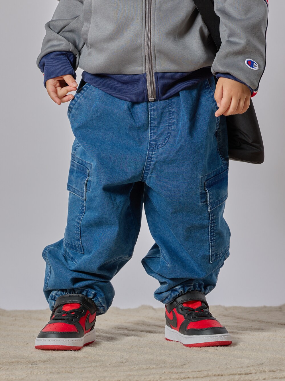 グレー系のブルゾン、ブルー系のカーゴパンツ、レッド系のスニーカーを着用したキッズの秋コーディネートの5枚目の写真