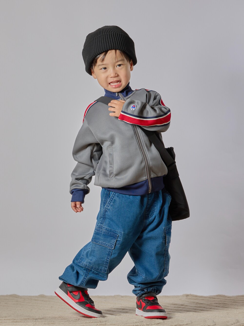 グレー系のブルゾン、ブルー系のカーゴパンツ、レッド系のスニーカーを着用したキッズの秋コーディネートの3枚目の写真