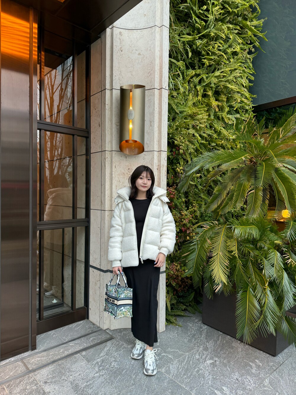 ブラック系のワンピース、ホワイト系のダウンジャケット/コート、シルバー系のスニーカーを着用したレディースの春コーディネートの3枚目の写真