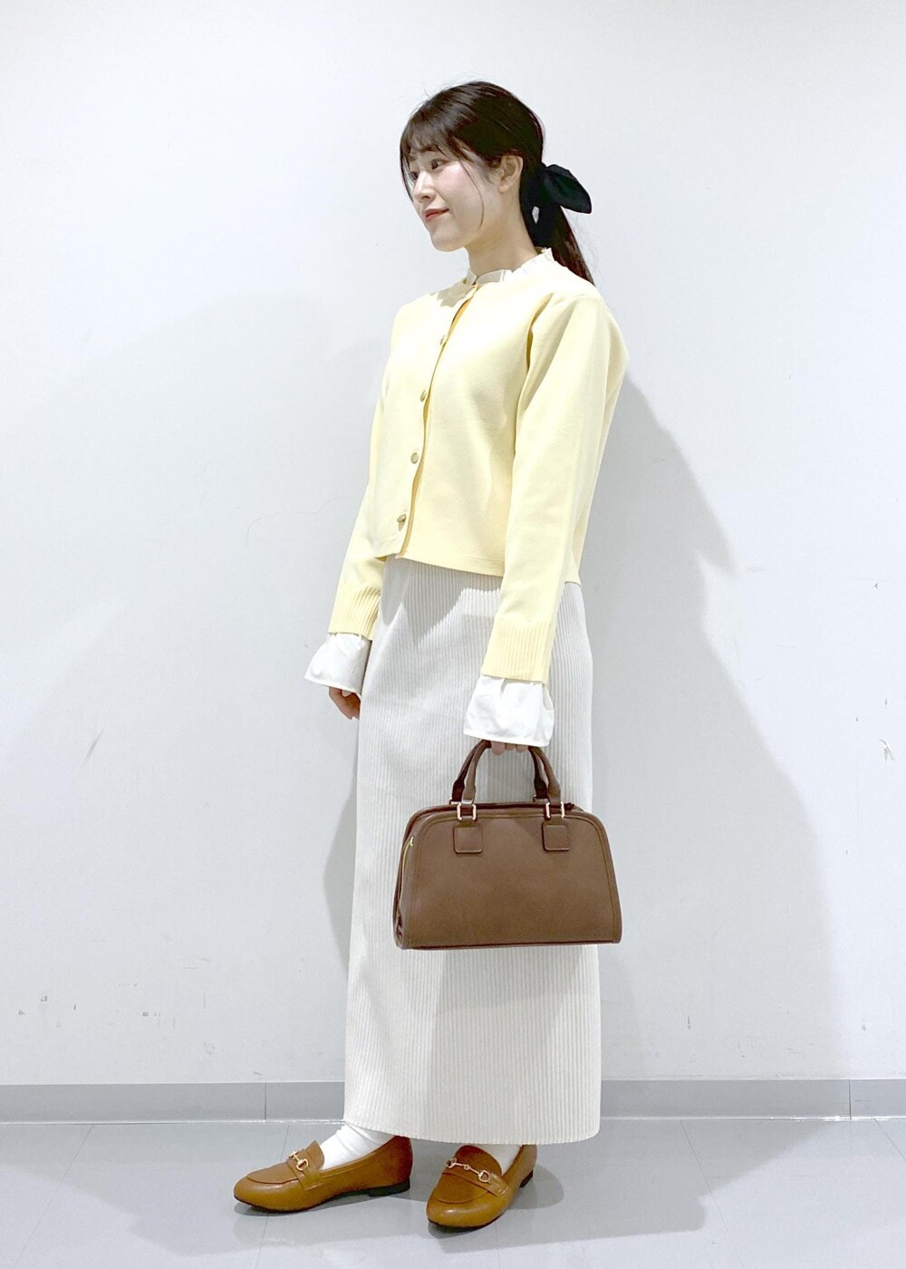 イエロー系のローファー、ブラウン系のボストンバッグ、ホワイト系のスカートを着用したレディースの冬コーディネートの4枚目の写真