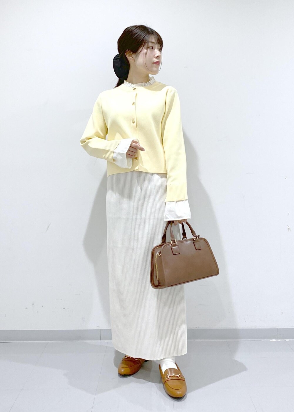 イエロー系のローファー、ブラウン系のボストンバッグ、ホワイト系のスカートを着用したレディースの冬コーディネートの3枚目の写真