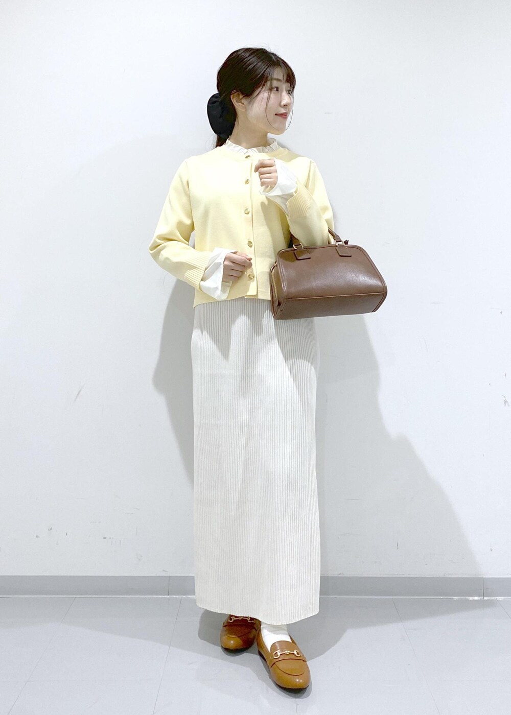 イエロー系のローファー、ブラウン系のボストンバッグ、ホワイト系のスカートを着用したレディースの冬コーディネートの2枚目の写真