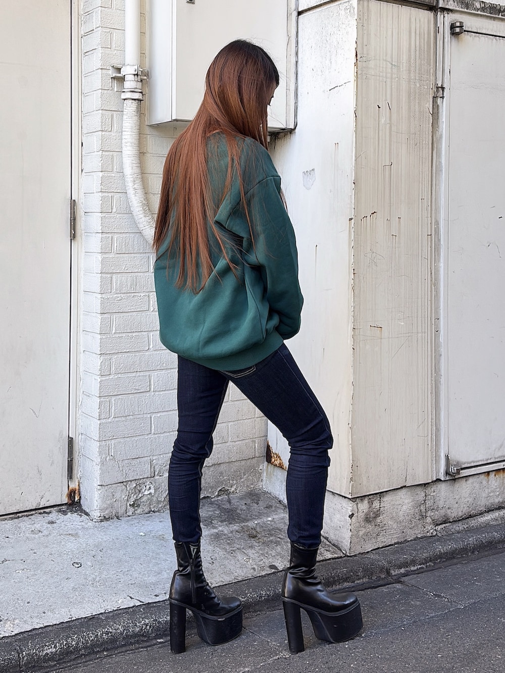 グリーン系のスウェット、ブルー系のデニムパンツ、ブラック系のブーツを着用したレディースの冬コーディネートの2枚目の写真