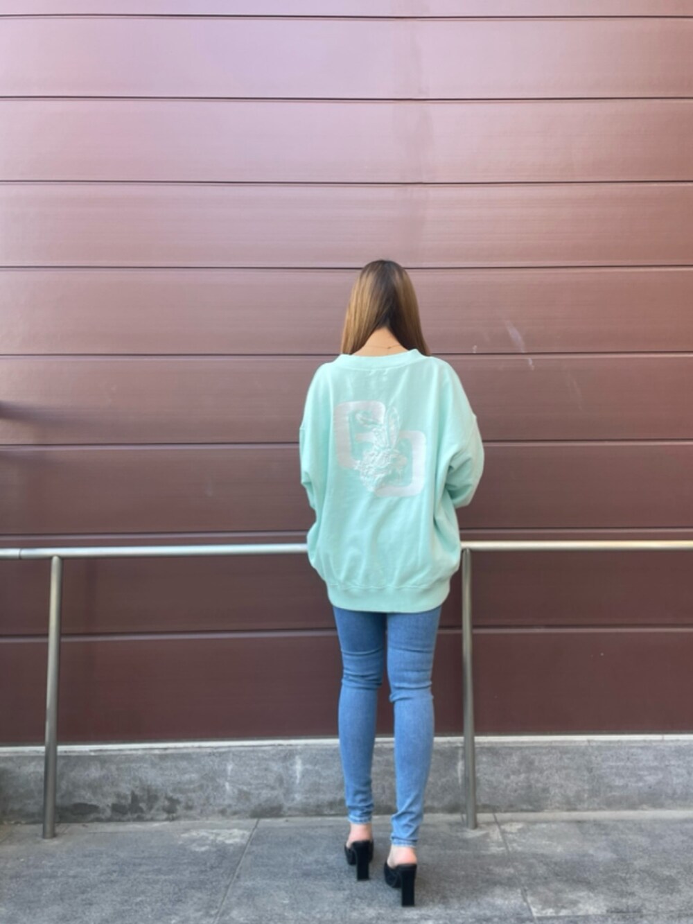 グリーン系のスウェット、ブルー系のデニムパンツ、ブラック系のパンプスを着用したレディースの春コーディネートの3枚目の写真