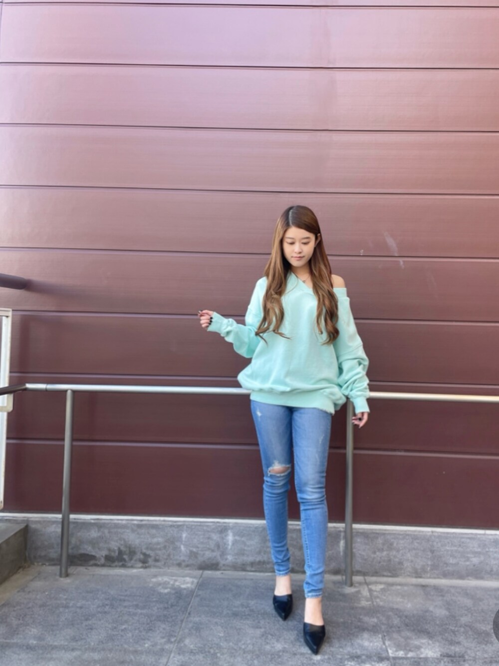 グリーン系のスウェット、ブルー系のデニムパンツ、ブラック系のパンプスを着用したレディースの春コーディネートの2枚目の写真