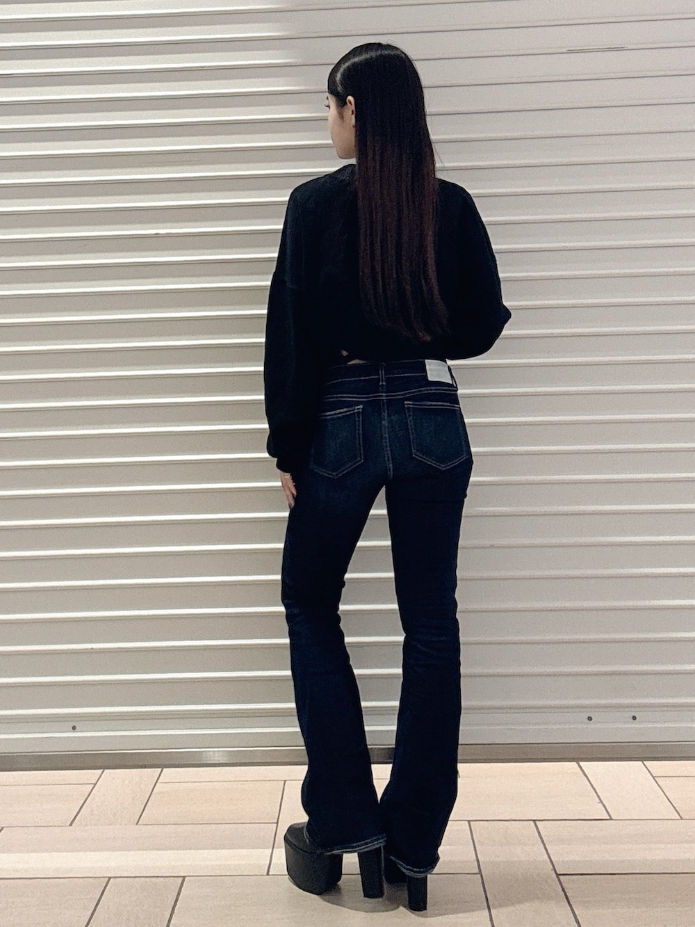 ブラック系のニット/セーター、ブルー系のデニムパンツ、ブラック系のブーツを着用したレディースの秋コーディネートの4枚目の写真