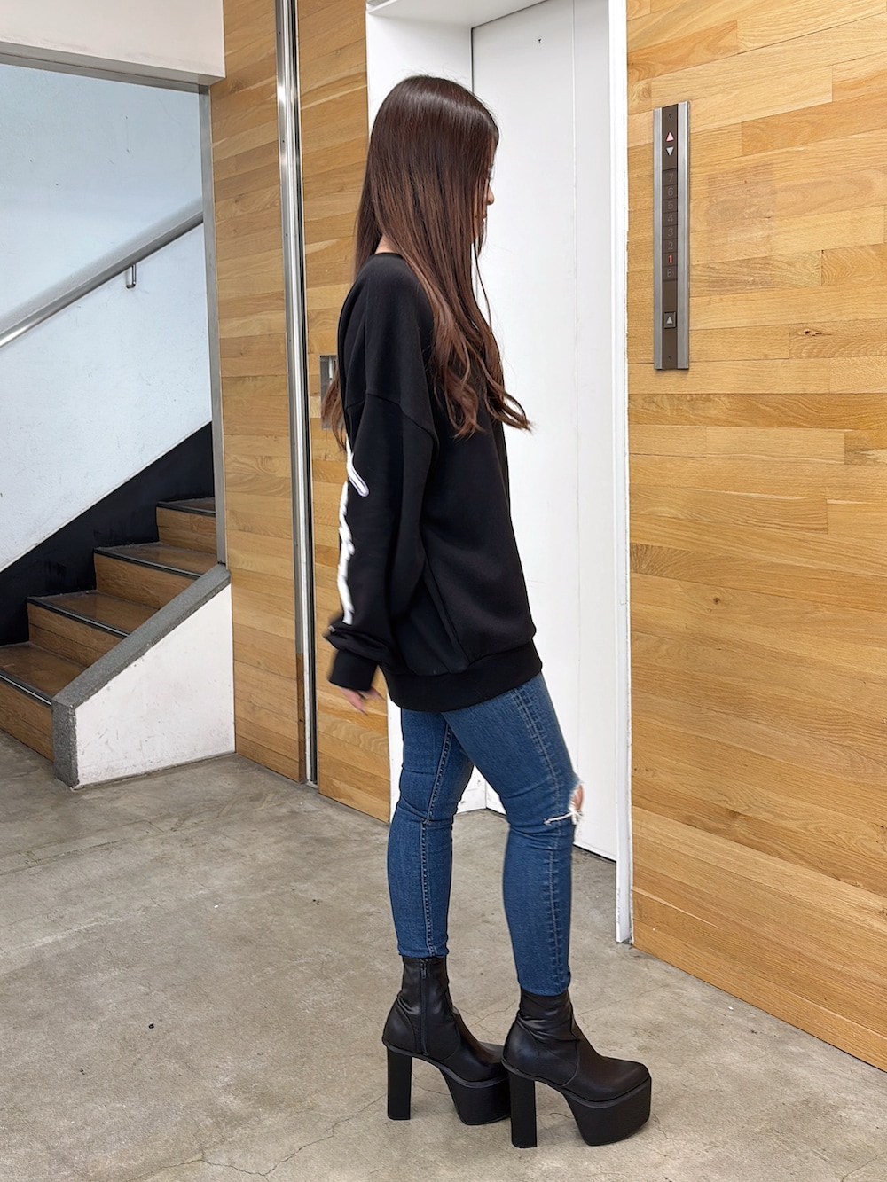 ブラック系のスウェット、ブルー系のデニムパンツ、ブラック系のブーツを着用したレディースの夏コーディネートの2枚目の写真