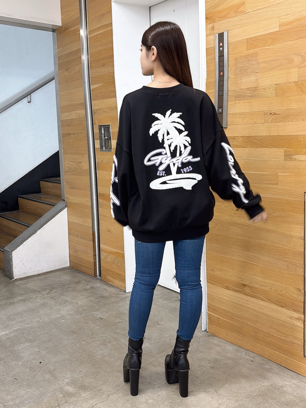 ブラック系のスウェット、ブルー系のデニムパンツ、ブラック系のブーツを着用したレディースの夏コーディネートの3枚目の写真