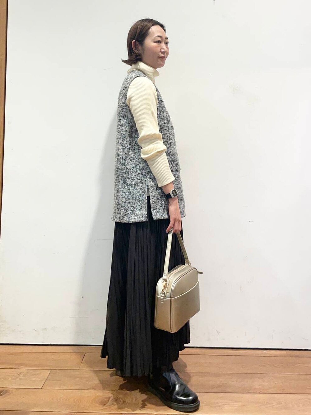 ゴールド系のショルダーバッグ、ホワイト系のニット/セーター、ブラック系のベストを着用したレディースの冬コーディネートの4枚目の写真