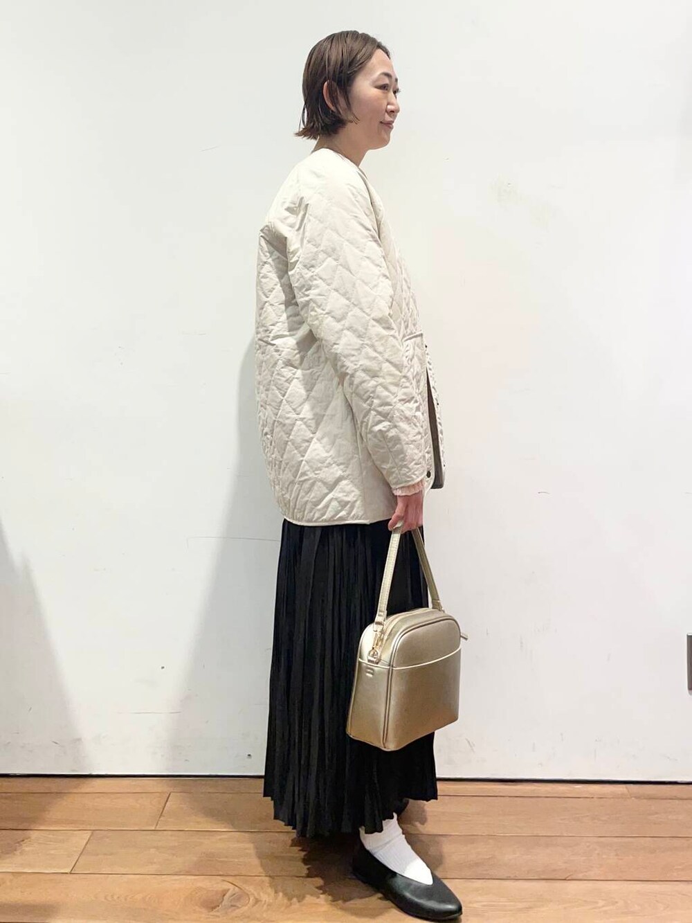 ゴールド系のショルダーバッグ、ブラック系のパンプス、ホワイト系のダウンジャケット/コートを着用したレディースの冬コーディネートの3枚目の写真