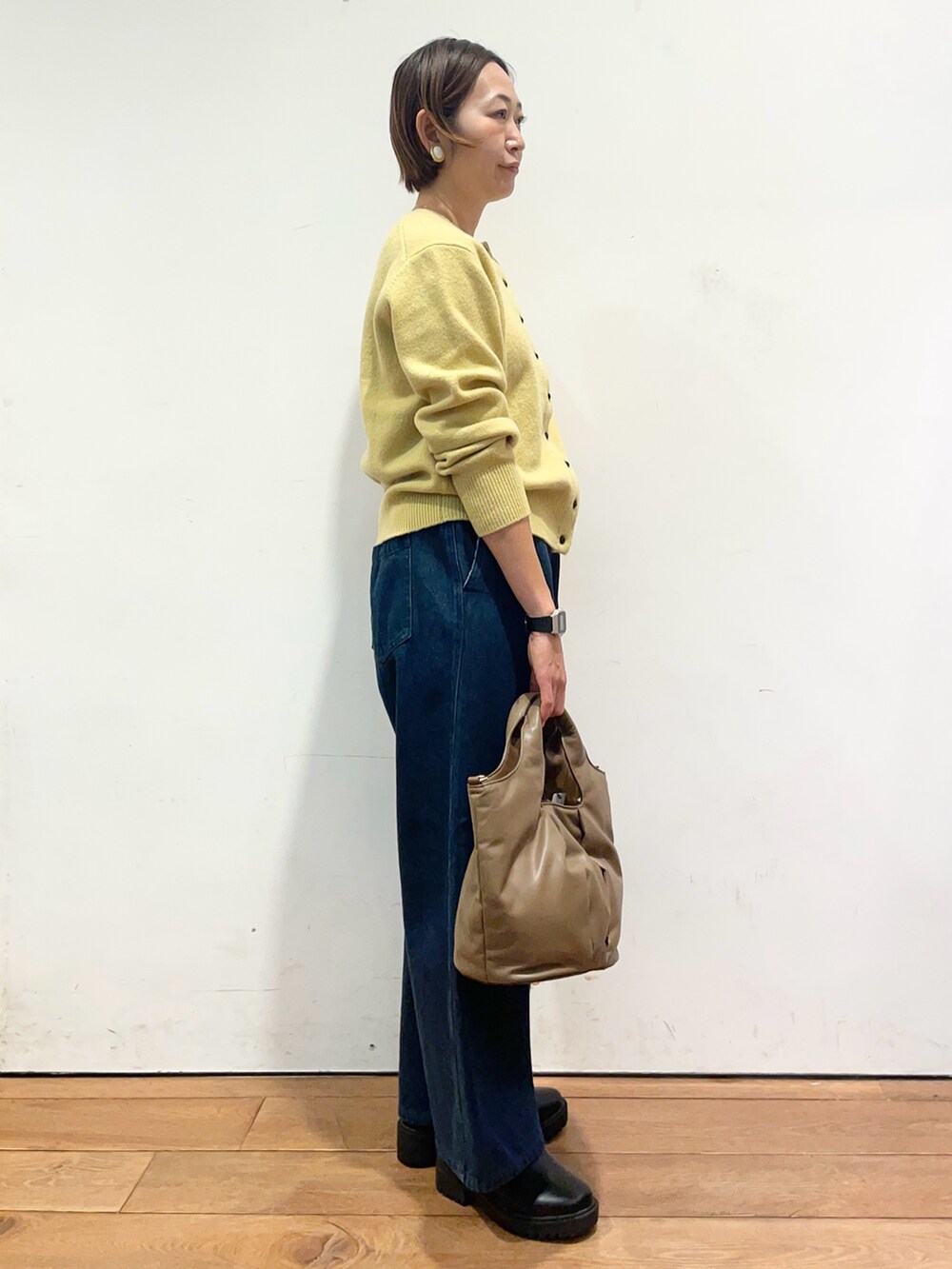 イエロー系のカーディガン/ボレロ、ブルー系のデニムパンツ、ブラウン系のハンドバッグを着用したレディースの秋コーディネートの4枚目の写真