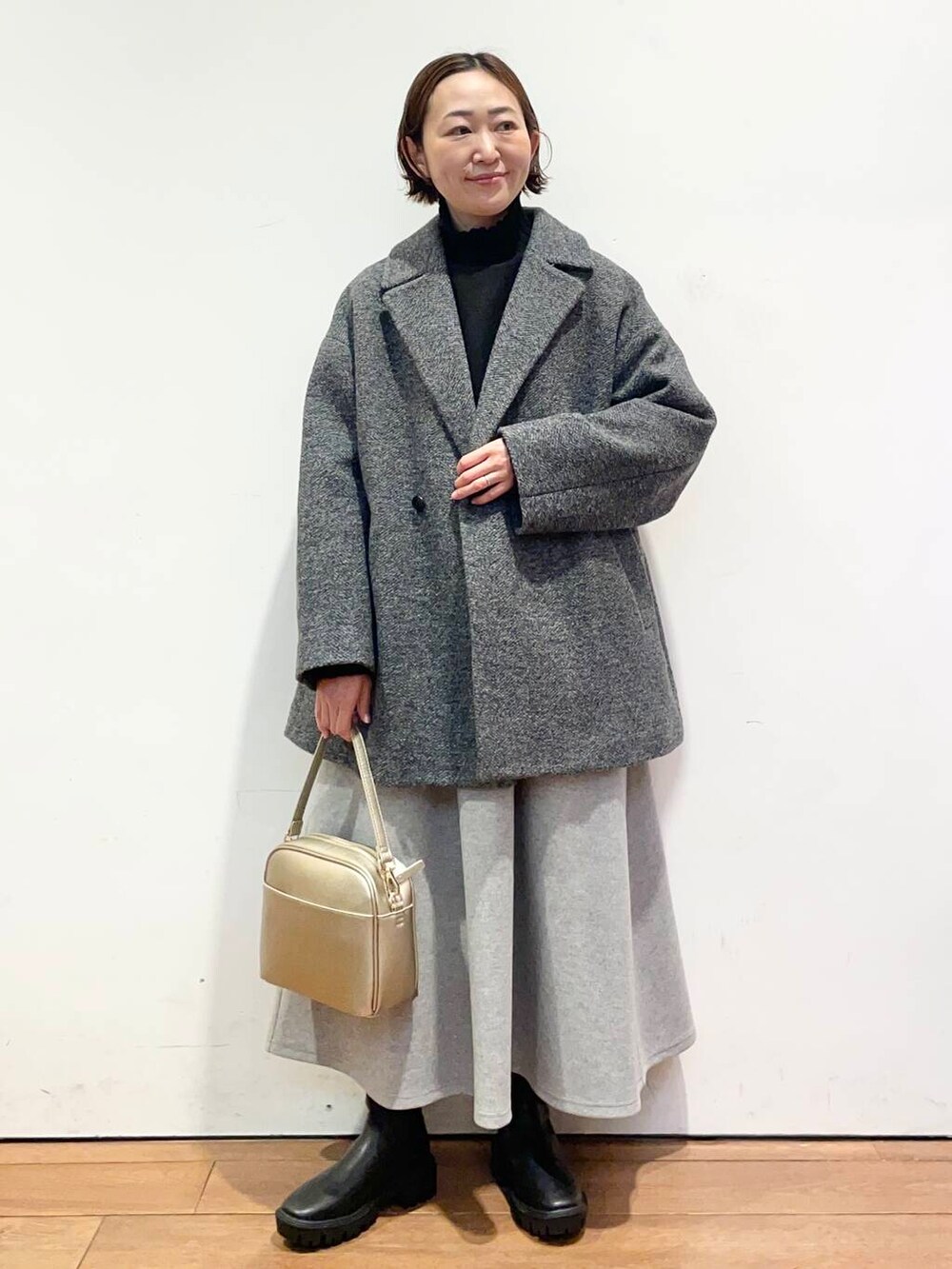 ゴールド系のショルダーバッグ、ブラック系のブーツ、グレー系のその他アウターを着用したレディースの冬コーディネートの2枚目の写真