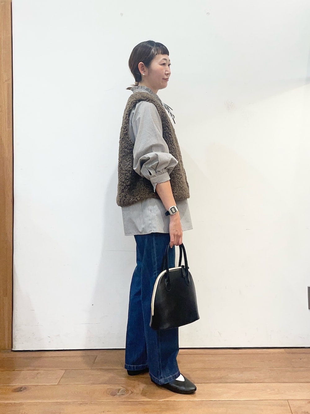 ブラック系のシャツ/ブラウス、ブラウン系のダウンベスト、ブルー系のデニムパンツを着用したレディースの秋コーディネートの4枚目の写真
