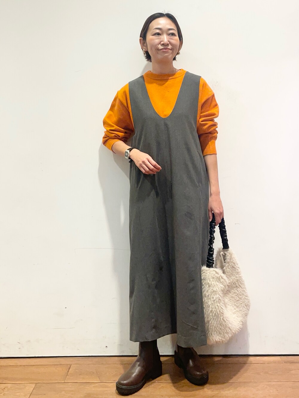 オレンジ系のニット/セーター、グレー系のワンピース、ブラウン系のブーツを着用したレディースの秋コーディネートの2枚目の写真