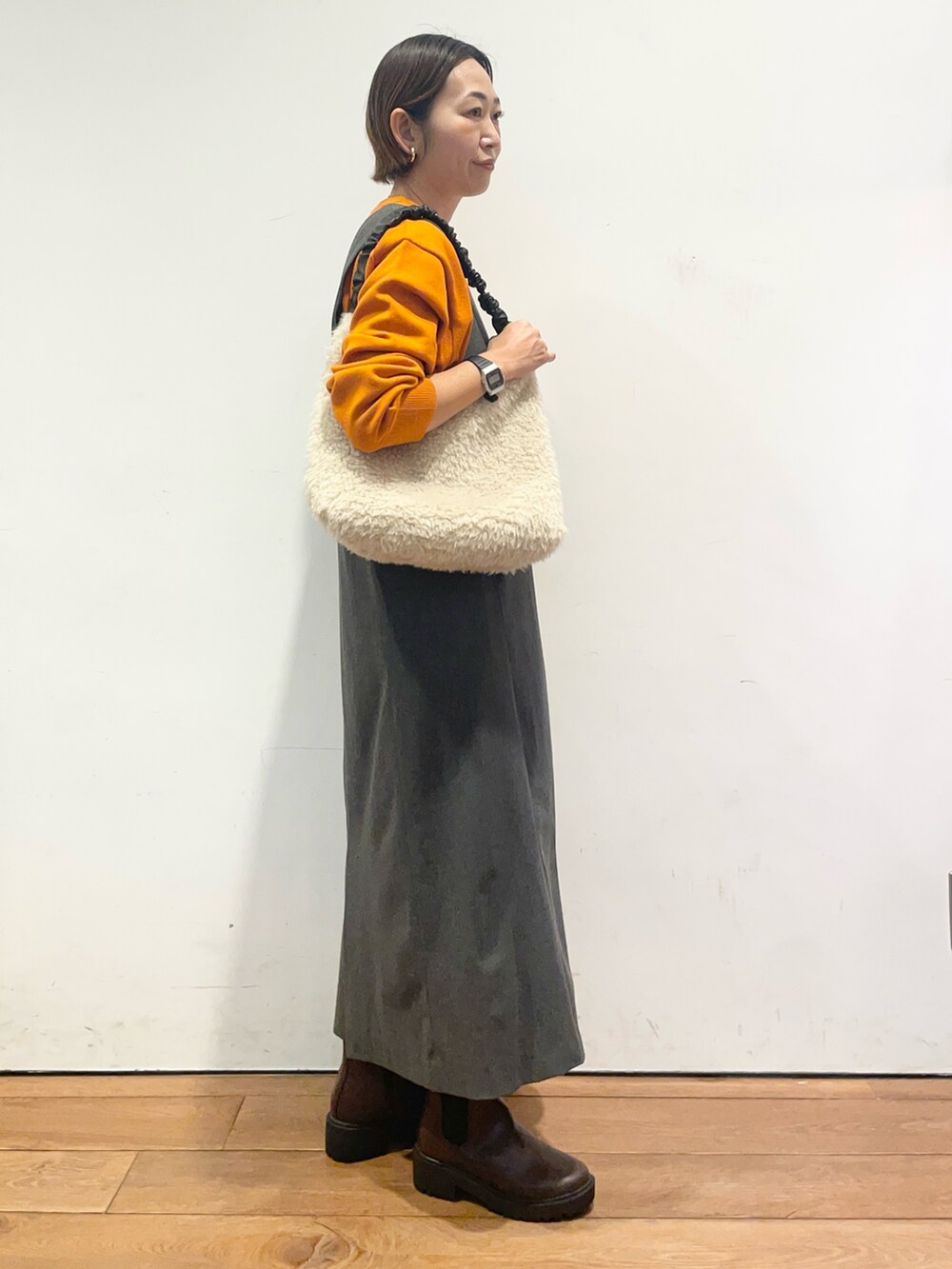 オレンジ系のニット/セーター、グレー系のワンピース、ブラウン系のブーツを着用したレディースの秋コーディネートの4枚目の写真