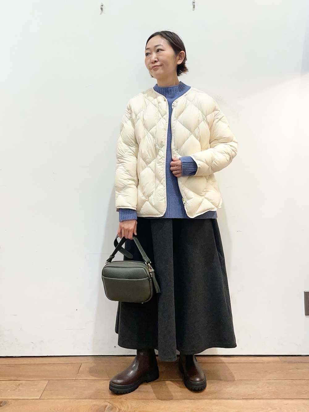 ホワイト系のダウンジャケット/コート、ブルー系のニット/セーター、グリーン系のショルダーバッグを着用したレディースの冬コーディネートの2枚目の写真