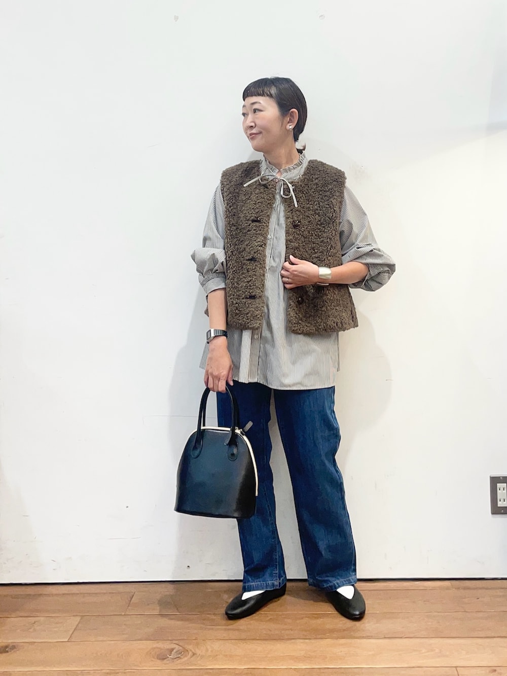 ブラック系のシャツ/ブラウス、ブラウン系のダウンベスト、ブルー系のデニムパンツを着用したレディースの秋コーディネートの3枚目の写真