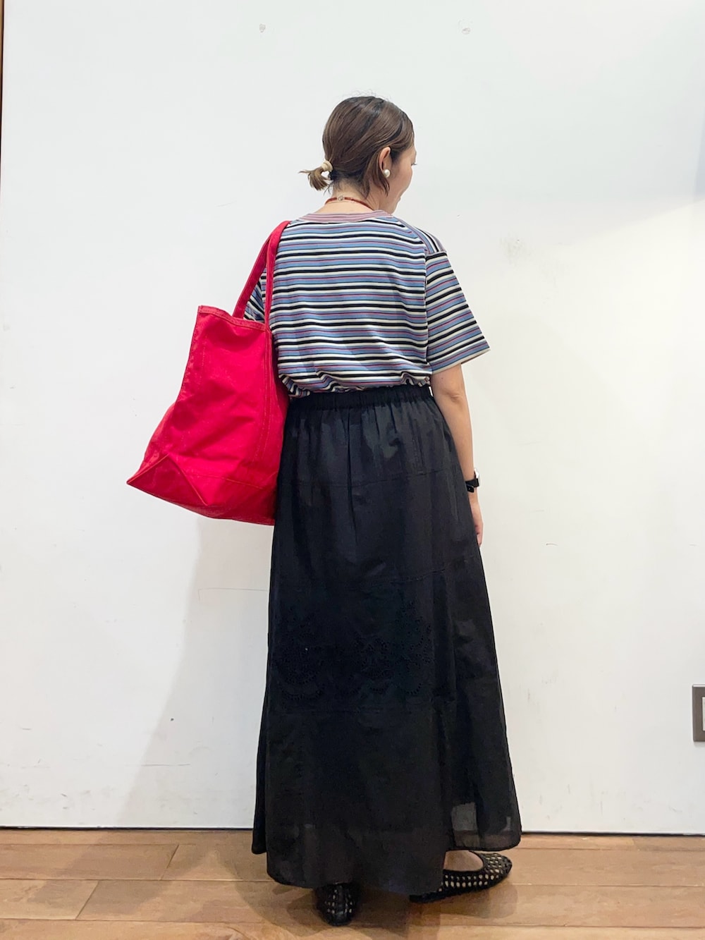 レッド系のトートバッグ、ブラック系のスカート、ブラック系のサンダルを着用したレディースの春コーディネートの5枚目の写真
