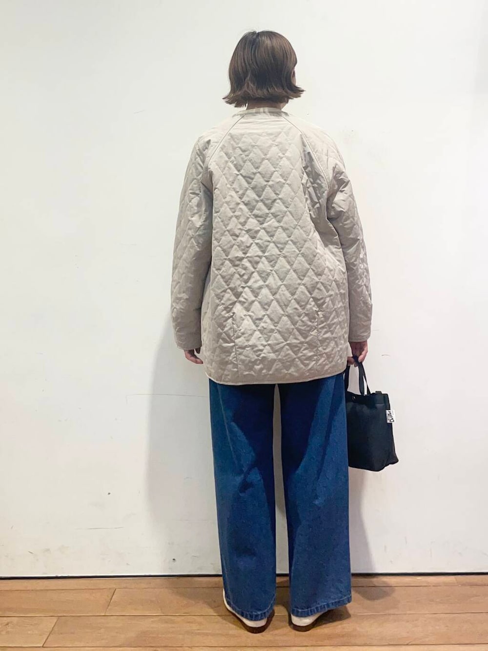 ブルー系のデニムパンツ、グレー系のダウンジャケット/コート、ブラック系のニット/セーターを着用したレディースの春コーディネートの5枚目の写真