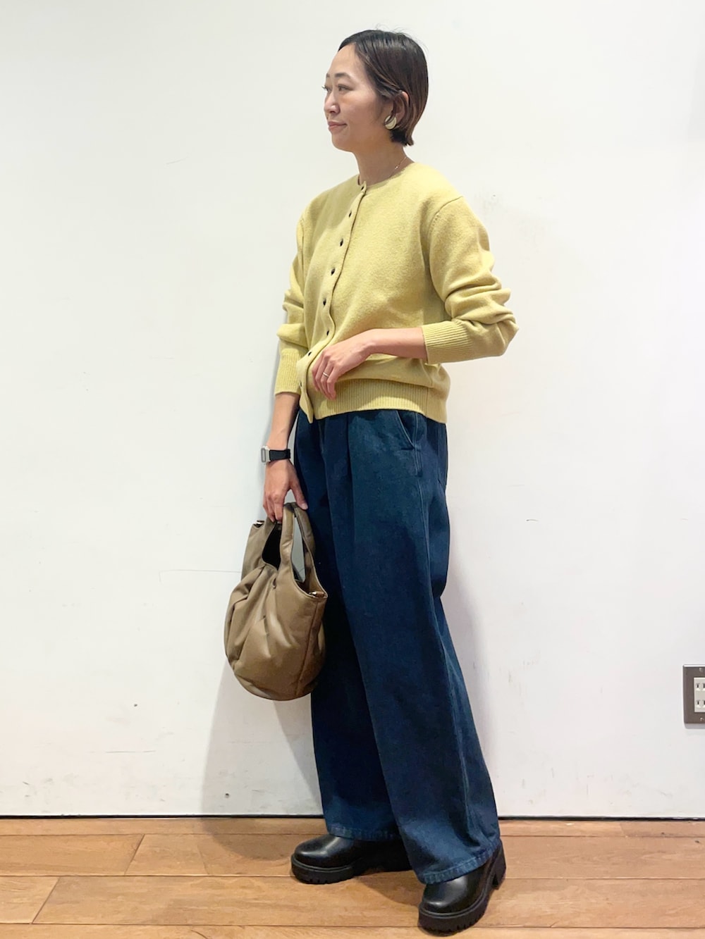 イエロー系のカーディガン/ボレロ、ブルー系のデニムパンツ、ブラウン系のハンドバッグを着用したレディースの秋コーディネートの3枚目の写真