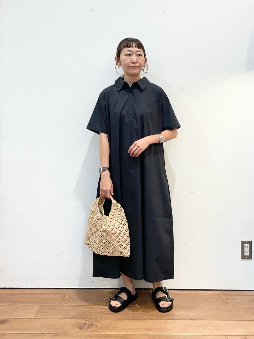 グレー系のワンピース、ベージュ系のハンドバッグ、ブラック系のサンダルを着用したレディースの夏コーディネートの2枚目の写真