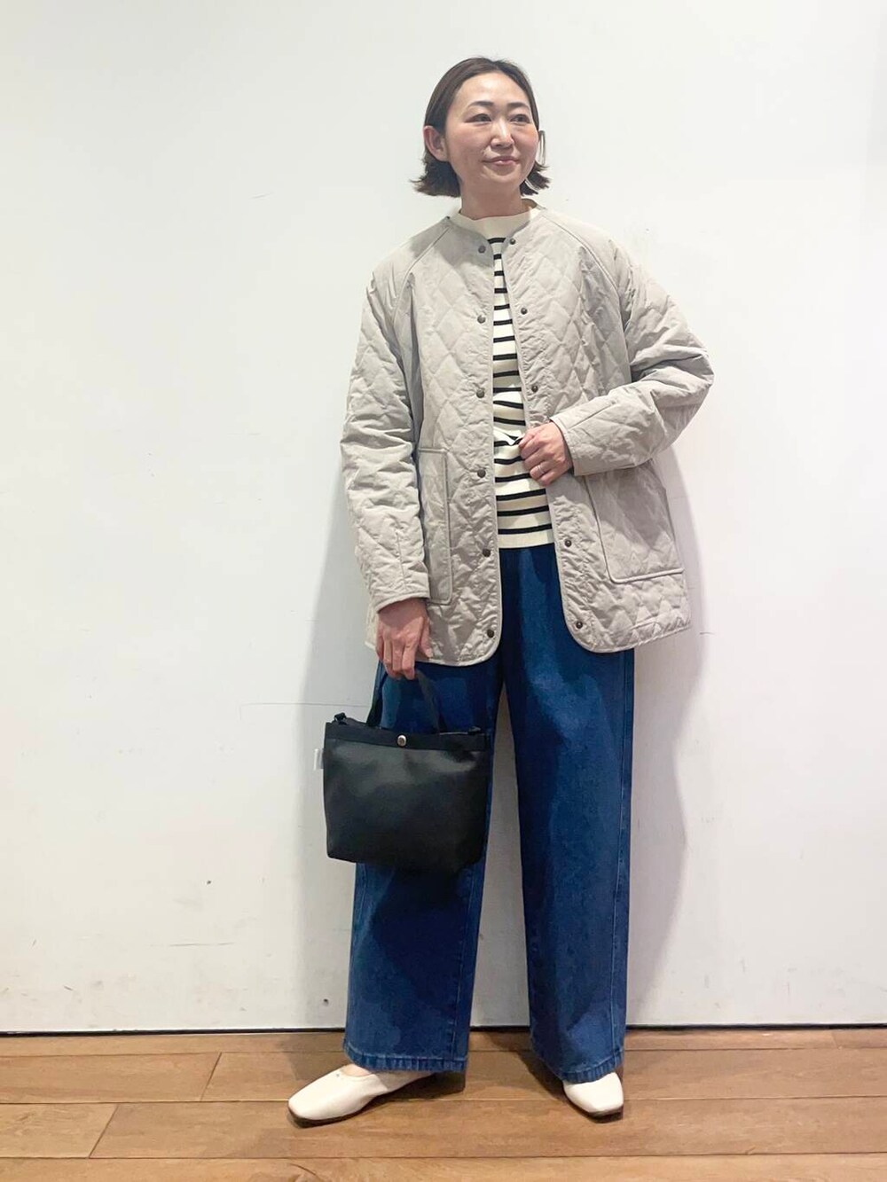 ブルー系のデニムパンツ、グレー系のダウンジャケット/コート、ブラック系のニット/セーターを着用したレディースの春コーディネートの2枚目の写真