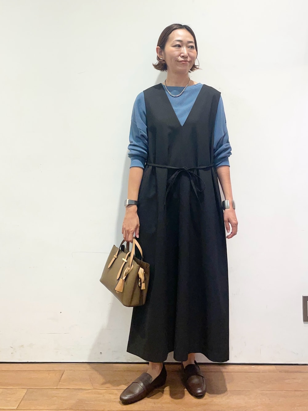 ブラック系のワンピース、ブルー系のTシャツ/カットソー、ブラウン系のパンプスを着用したレディースの秋コーディネートの2枚目の写真