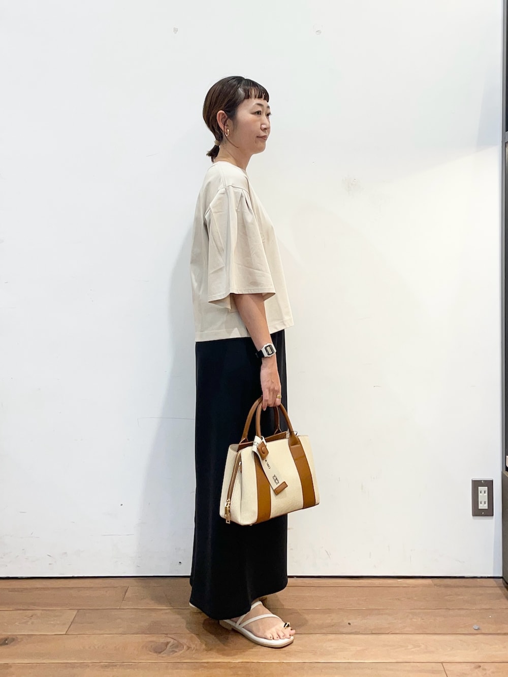 ベージュ系のTシャツ/カットソー、ブラック系のスカート、ホワイト系のハンドバッグを着用したレディースの夏コーディネートの3枚目の写真