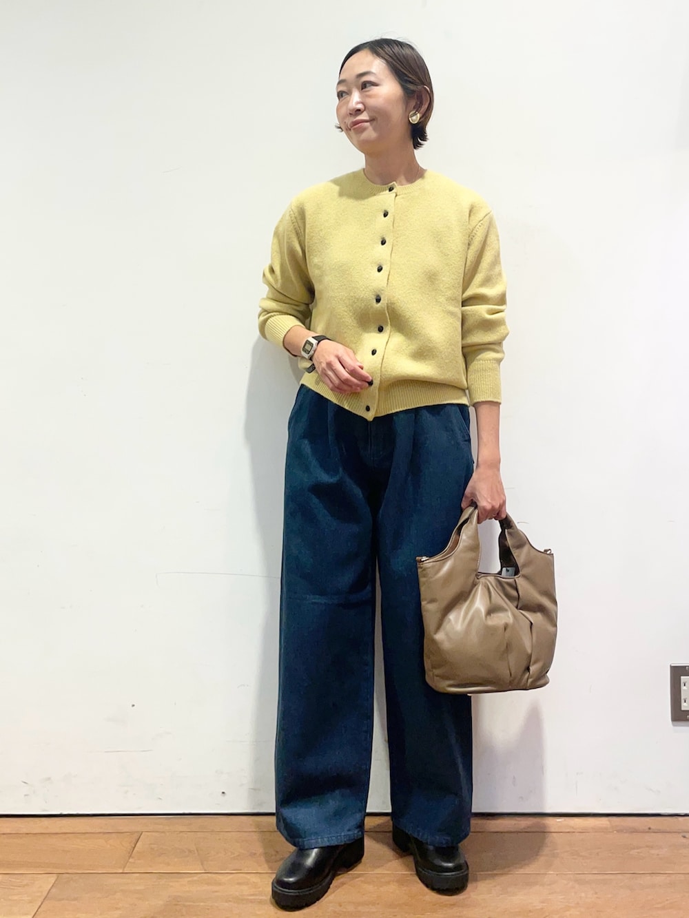 イエロー系のカーディガン/ボレロ、ブルー系のデニムパンツ、ブラウン系のハンドバッグを着用したレディースの秋コーディネートの2枚目の写真