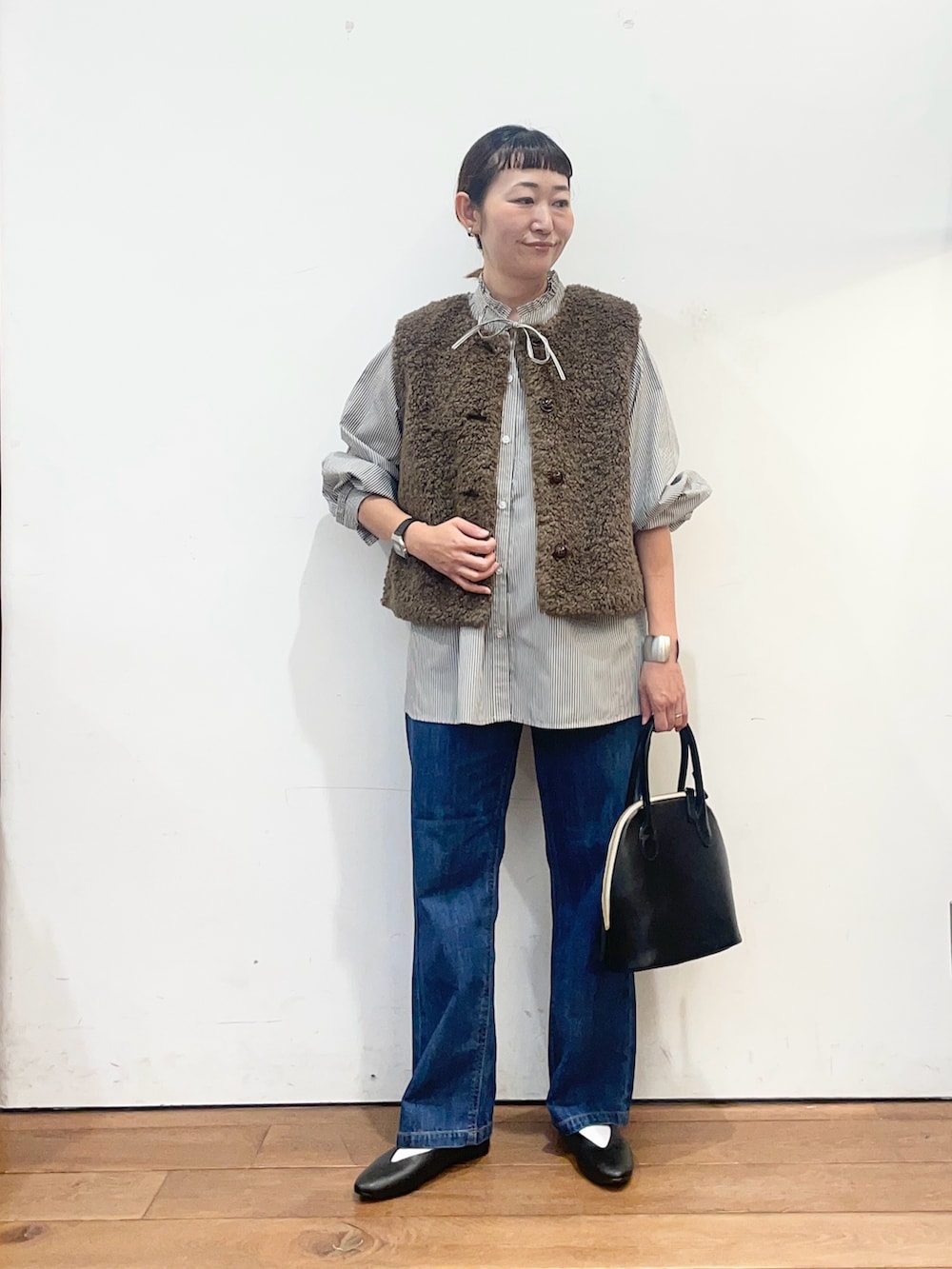 ブラック系のシャツ/ブラウス、ブラウン系のダウンベスト、ブルー系のデニムパンツを着用したレディースの秋コーディネートの2枚目の写真