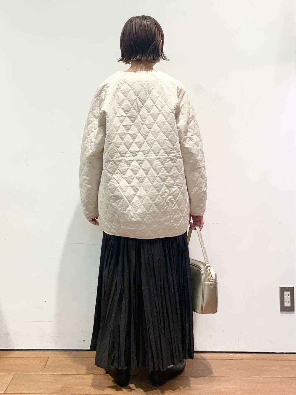 ゴールド系のショルダーバッグ、ブラック系のパンプス、ホワイト系のダウンジャケット/コートを着用したレディースの冬コーディネートの4枚目の写真