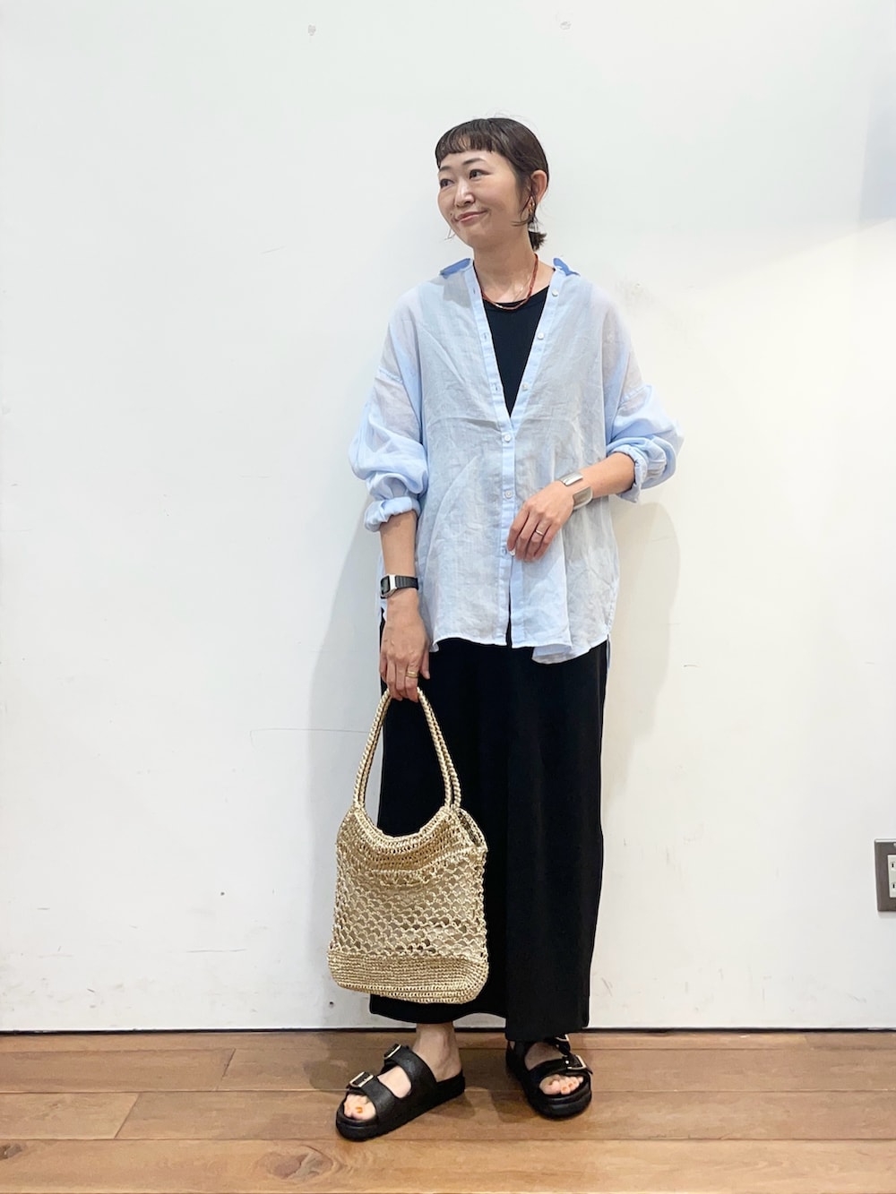 ブルー系のシャツ/ブラウス、ブラック系のワンピース、ゴールド系のトートバッグを着用したレディースの夏コーディネートの2枚目の写真