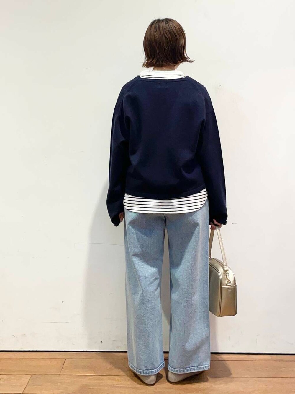 ゴールド系のショルダーバッグ、ブルー系のデニムパンツ、グレー系のパンプスを着用したレディースの冬コーディネートの5枚目の写真