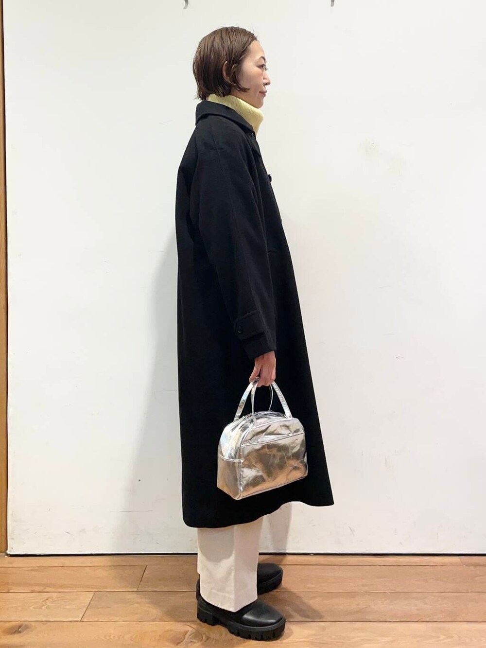 ブラック系のその他アウター、イエロー系のニット/セーター、ブラック系のブーツを着用したレディースの冬コーディネートの4枚目の写真