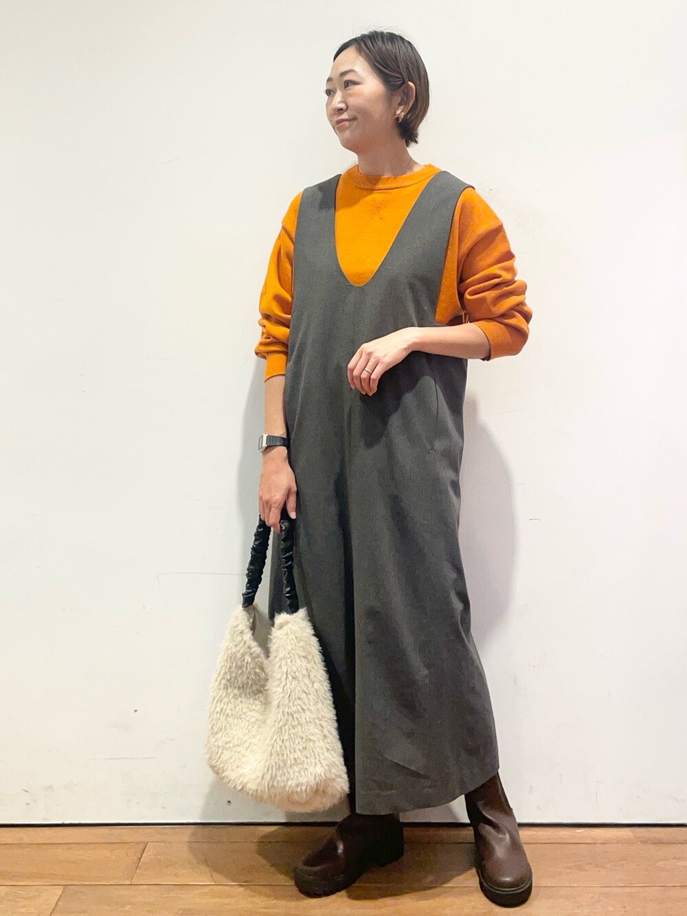 オレンジ系のニット/セーター、グレー系のワンピース、ブラウン系のブーツを着用したレディースの秋コーディネートの3枚目の写真