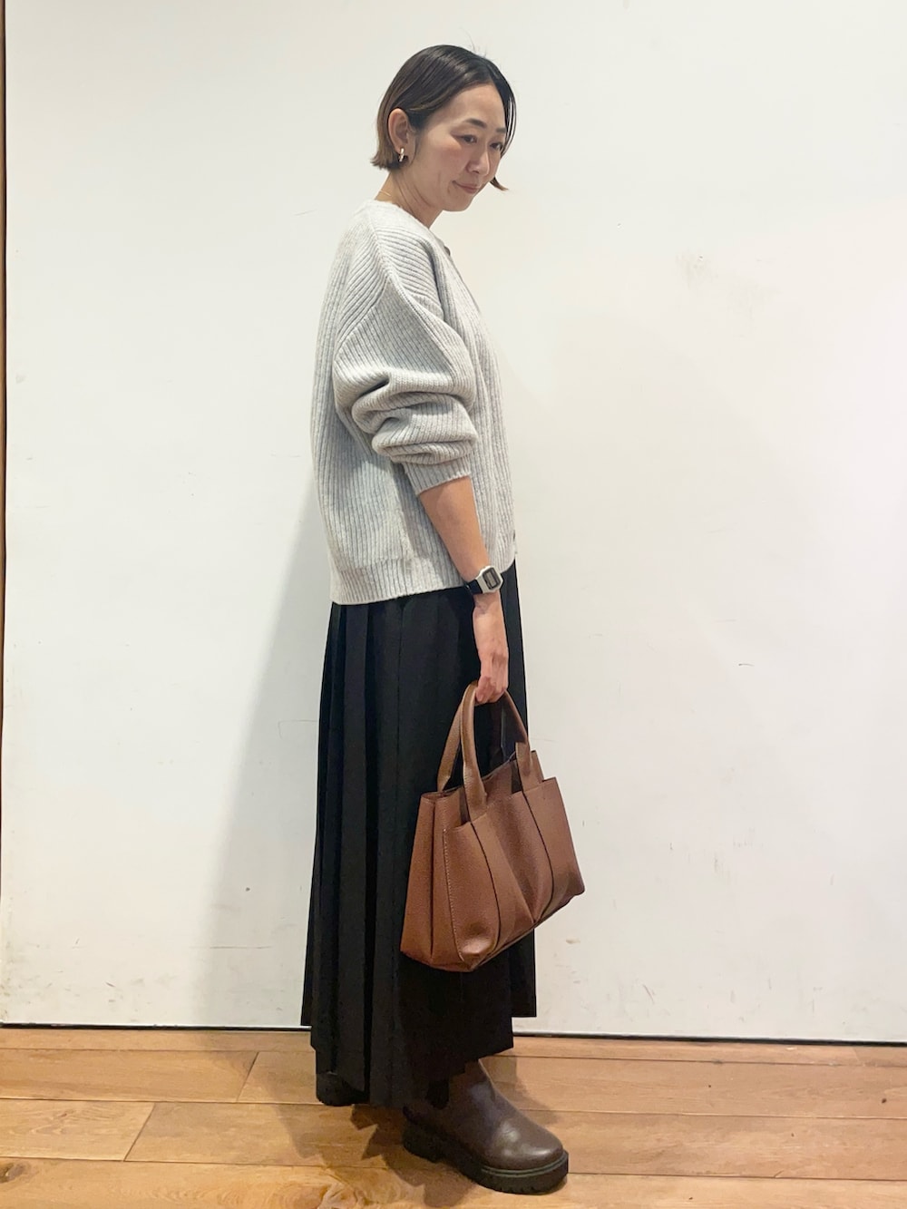 ブラック系のスカート、ブラウン系のトートバッグ、ブラウン系のブーツを着用したレディースの秋コーディネートの4枚目の写真