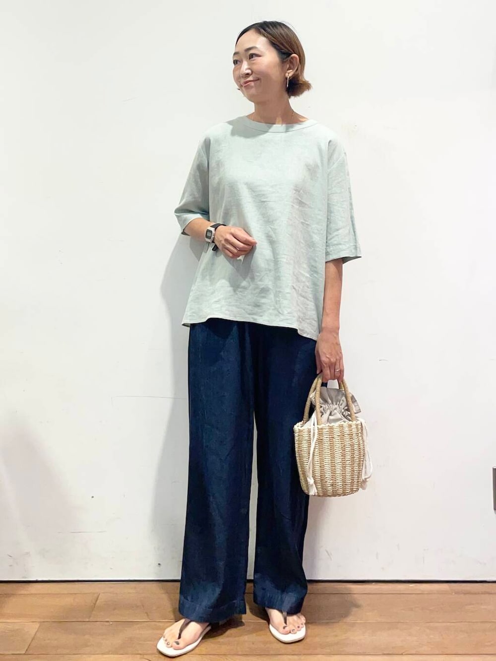 グレー系のハンドバッグ、ブラウン系のサンダル、ブルー系のデニムパンツを着用したレディースの夏コーディネートの2枚目の写真