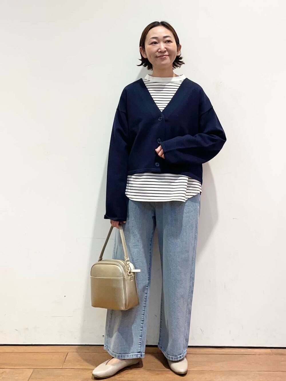 ゴールド系のショルダーバッグ、ブルー系のデニムパンツ、グレー系のパンプスを着用したレディースの冬コーディネートの3枚目の写真